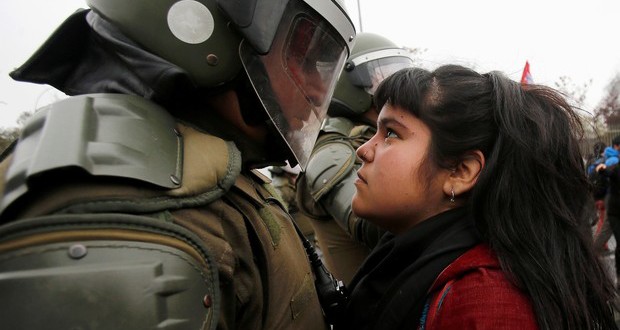 Jovem encara policial em Santiago neste domingo (11) (Foto: Carlos Vera/Reuters)