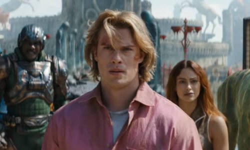 Homem de cabelo loiro e camisa rosa está no centro da imagem, com mulher de cabelo longo e escuro atrás dele à direita. À esquerda, dois personagens com armaduras futuristas e um tigre com listras verdes e amarelas está à direita. Cenário ao fundo inclui estruturas e estátuas em ambiente aberto.