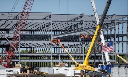 Workers use cranes and other machinery to place metal beams during construction.
