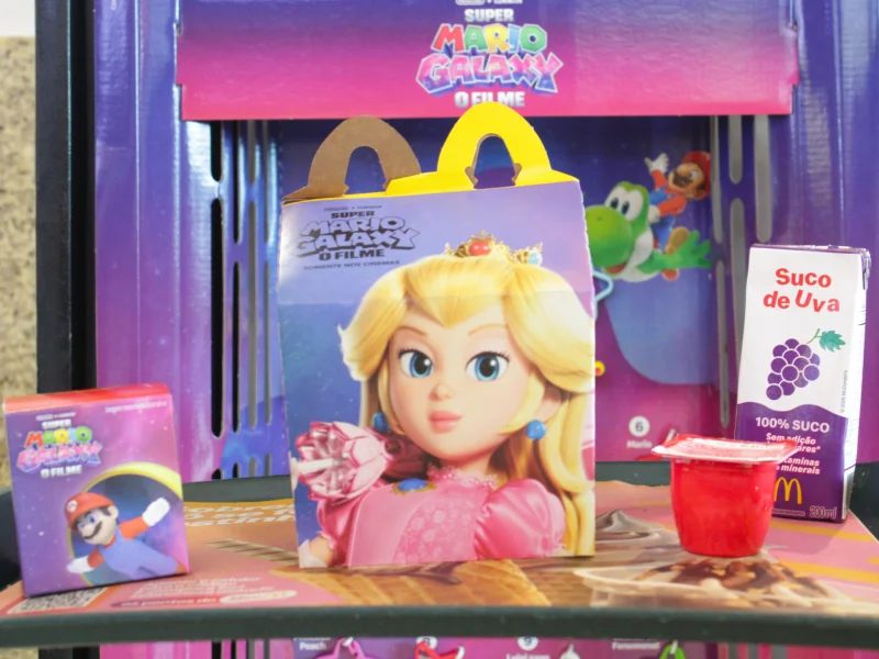 Caixa de McLanche Feliz com o rosto da Princesa Peach, acompanhada de suco de uva, maçã e uma pequena embalagem do Mario.