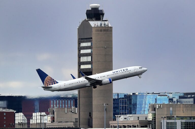 The Logan Airport control tower looms large as a United Airlines jet takes off in Boston.