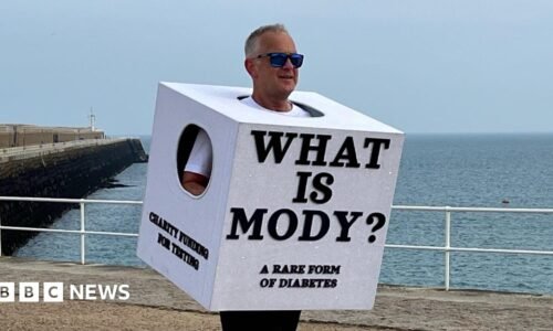 Richard is running long a seaside promenade wearing a large white cube costume with the text ‘WHAT IS MODY? A RARE FORM OF DIABETES,’ with the ocean and a pier behind him