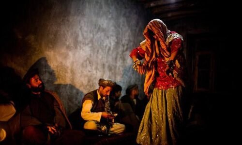 A boy dressed in women's clothing performs before a group of men in a dimly lit room in Afghanistan, illustrating the practice of bacha bazi. (Photo credit: Getty Images)