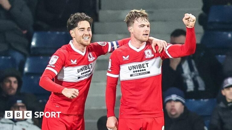 Hayden Hackney, wearing the captain's armband on his left arm, has his left hand on Tommy Conway's left shoulder. Conway has his left fist clenched after Middlesbrough had scored.