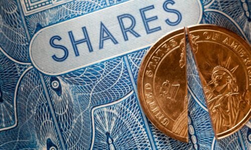 A U.S. dollar coin split in half that's been placed atop a paper stock certificate for shares in a public company.