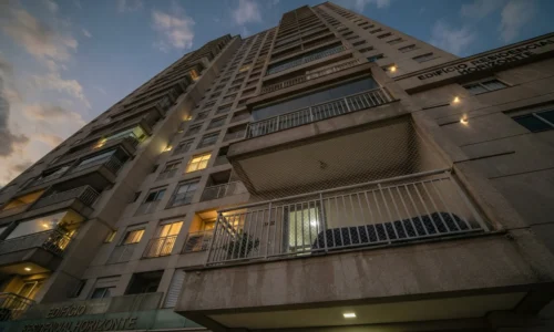 Prédio residencial alto visto de baixo com sacada do 14º andar e rede de proteção ao entardecer