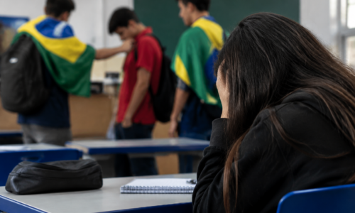 Estudantes representados por mochilas e cadernos em ambiente escolar, sem rostos visíveis.